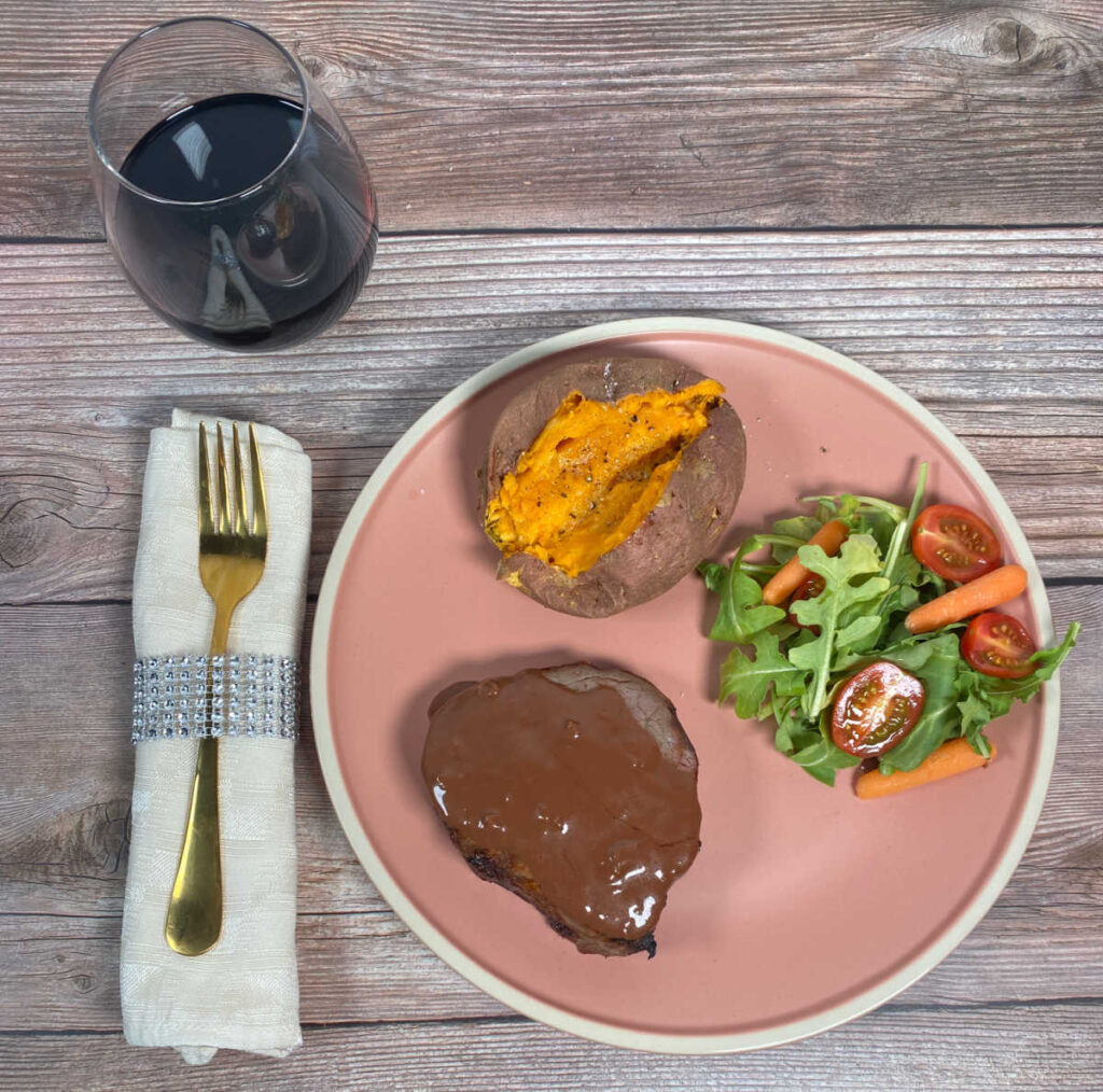 Overhead image of steak with side dishes and a glass of red wine.