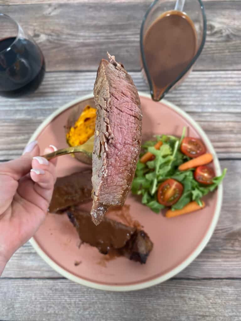 Slice of steak, cooked medium, held up on a fork above the rest of the plated food.