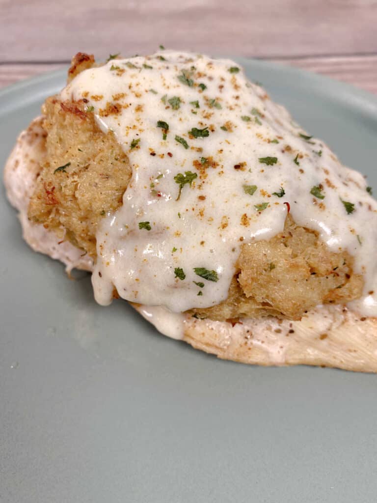 Chicken topped with crab imperial and cream sauce sits on a plate. 