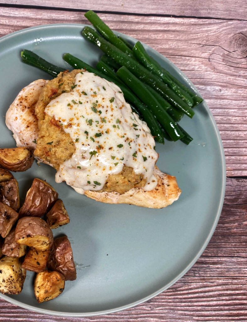 Image of plated recipe with cream sauce dripping down the crab and chicken. Potatoes and green beans fill the plate as side dishes. 