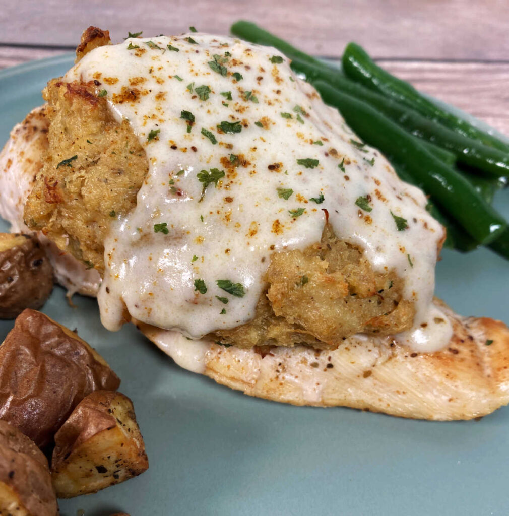 Chicken cutlet topped with crab imperial and cream sauce sits on a light green plate. 