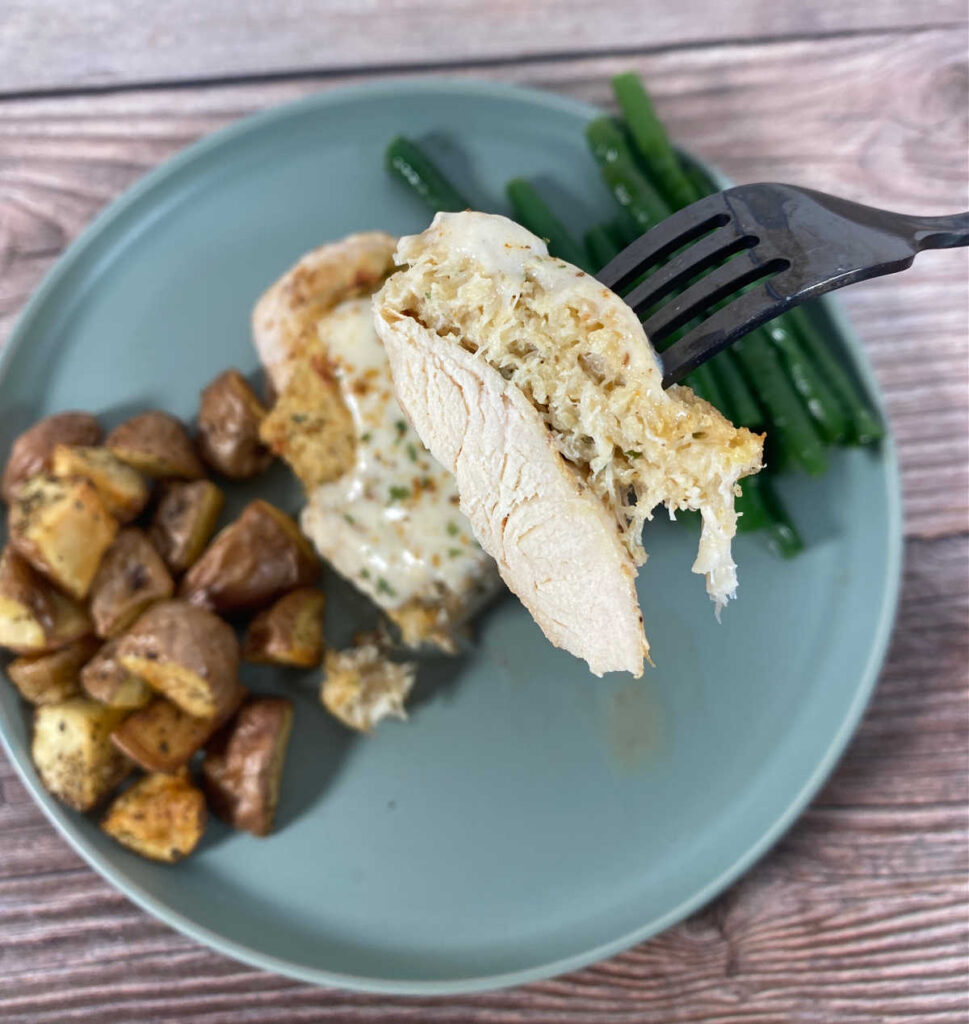 Close up, overhead image of piece of chicken with crab meat on a fork, hovering above the rest of the dish. 