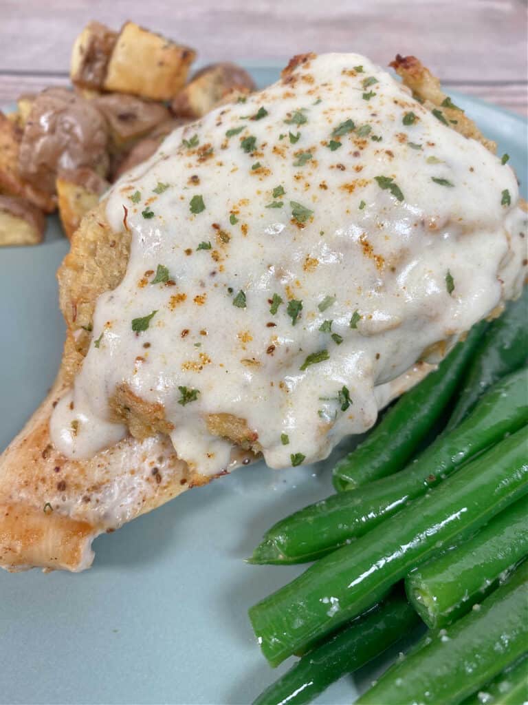 Close up image of recipe with cream sauce coating the crab and chicken. Steamed green beans sit off to the side. 