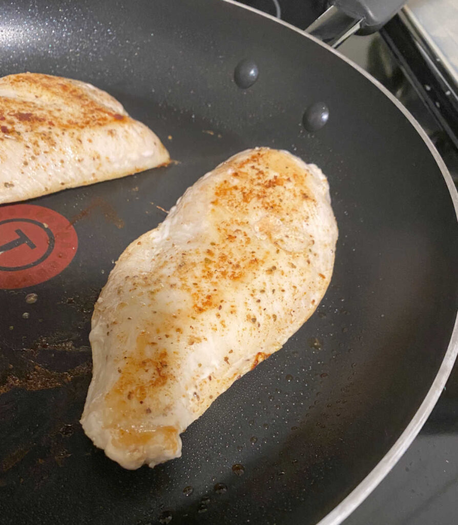 Process shot - seasoned chicken cutlets cooking in a skillet. 