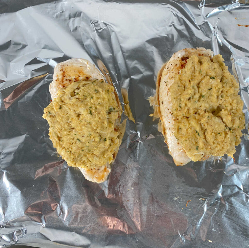 Process shot - mostly cooked chicken transferred to baking sheet and topped with crab, awaiting additional baking.