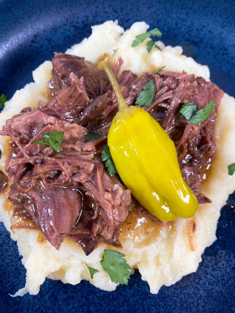 Close up image of pot roast, served over mashed potatoes and sprinkled with parsley.