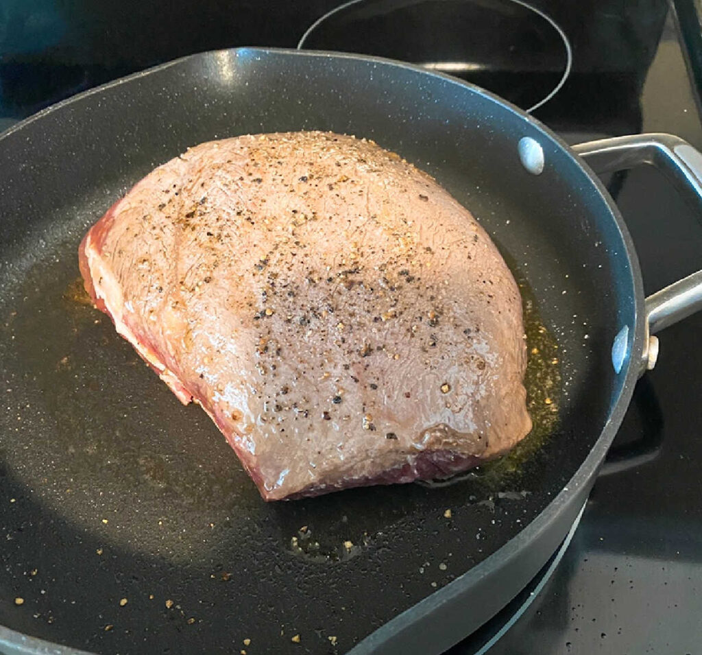 Process shot - roast in a skillet being browned on all sides. 