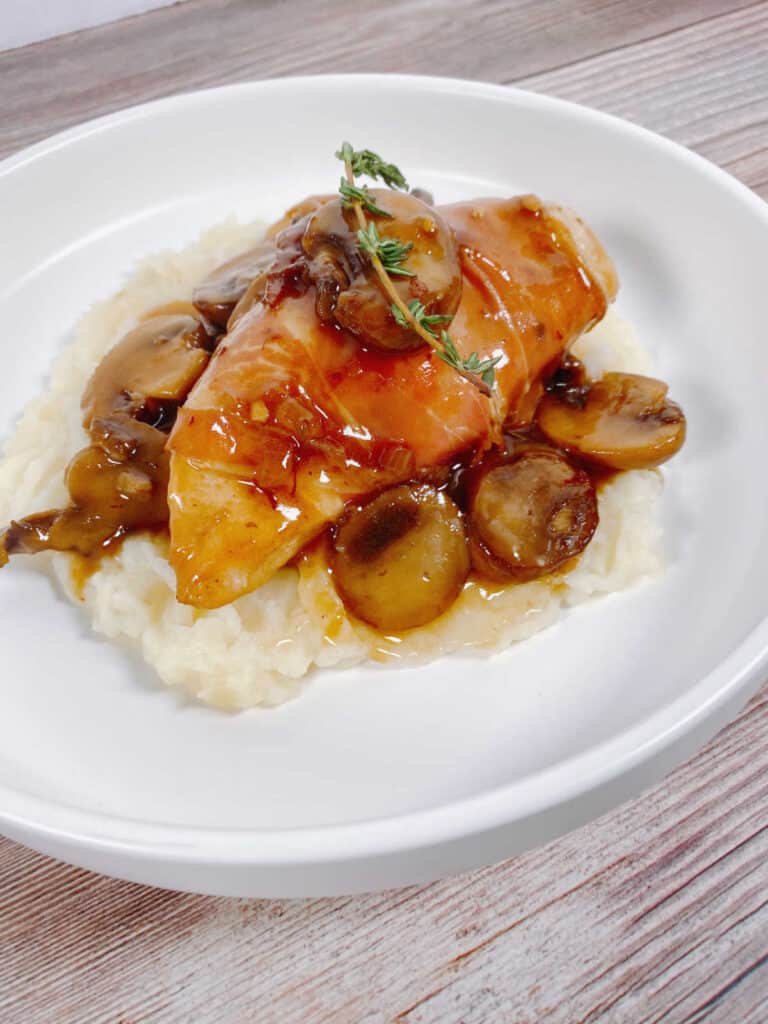 Image from the side showing mushroom sauce on top of mashed potatoes with chicken on top of that. 