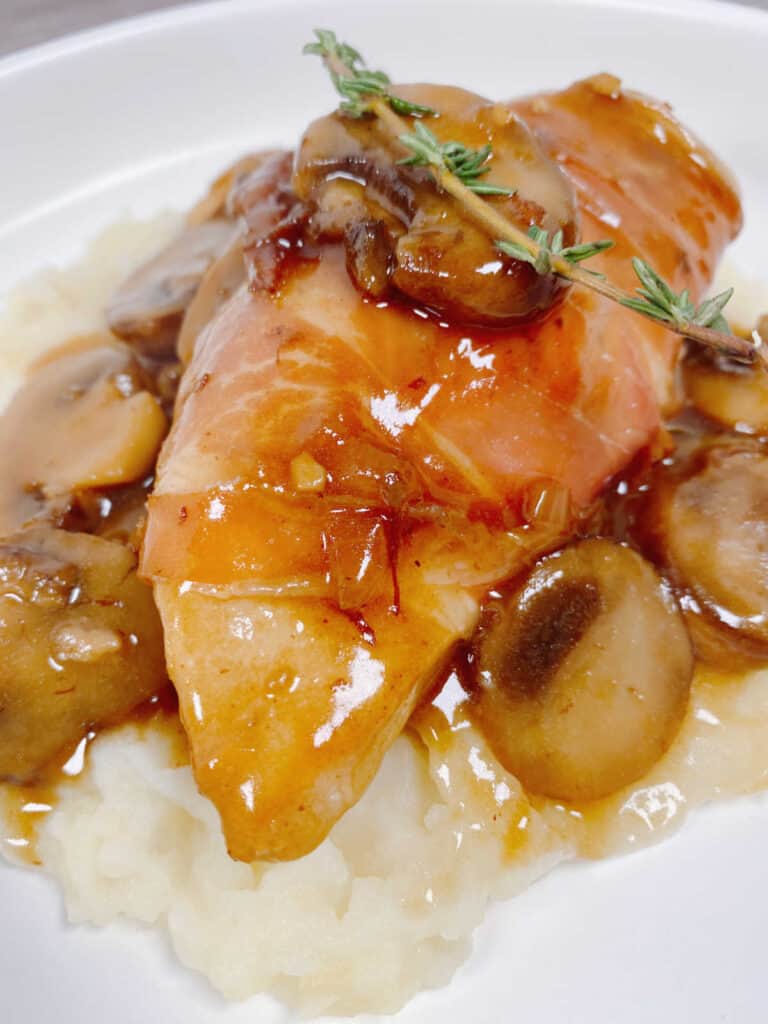 close up image of the chicken garnished with thyme, on top of the mushroom sauce. 