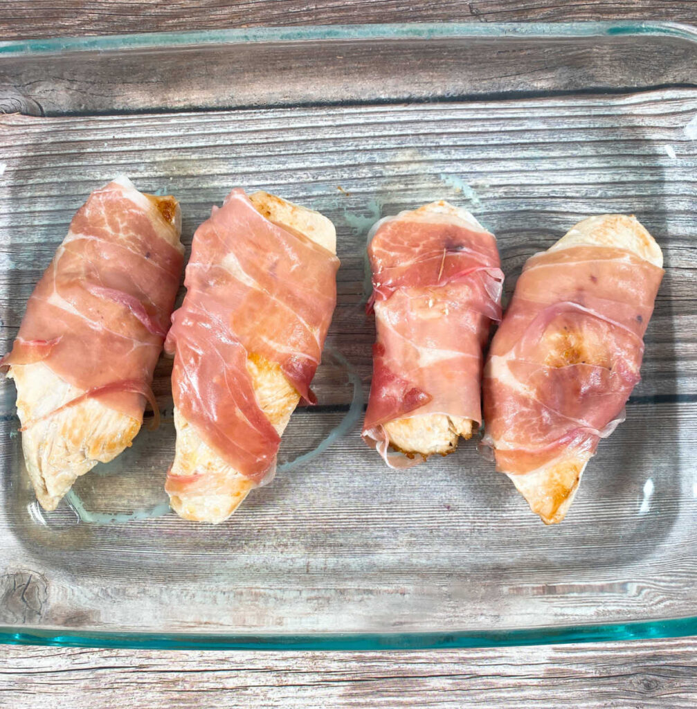 Process shot - prosciutto wrapped chicken in a glass baking dish ready to go into the oven. 