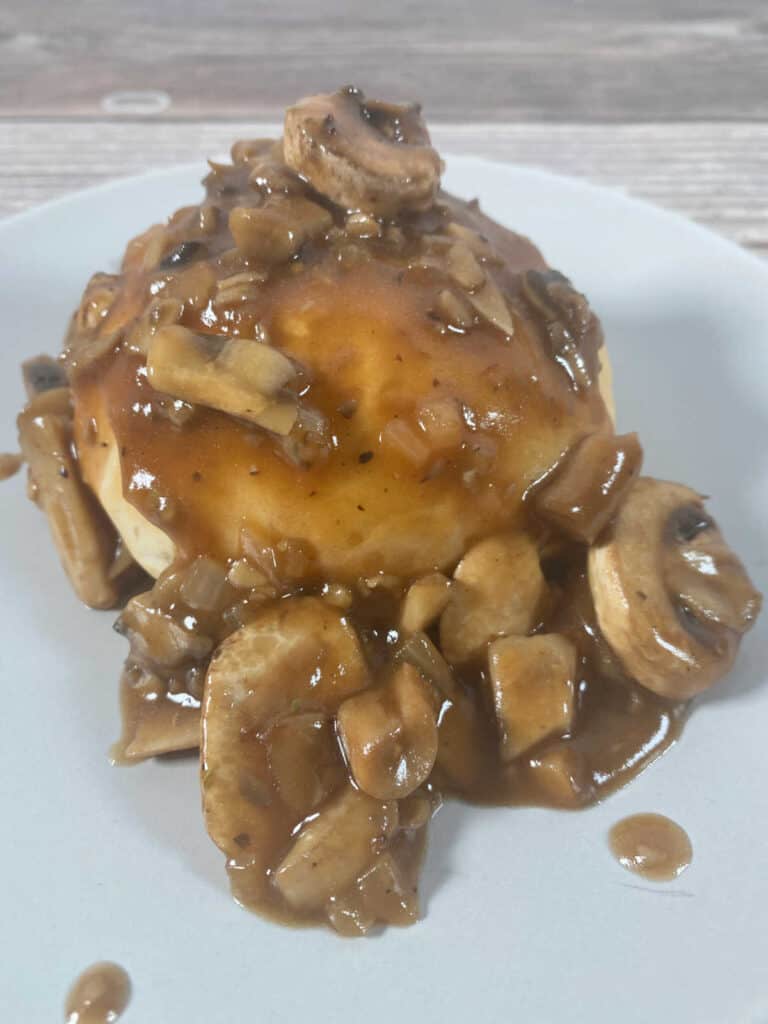 close up of beef wellington bomb, with mushroom sauce on top on a white plate.