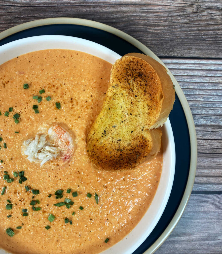 Overhead image of bisque in shallow white bowl, garlic bread resting on soup.