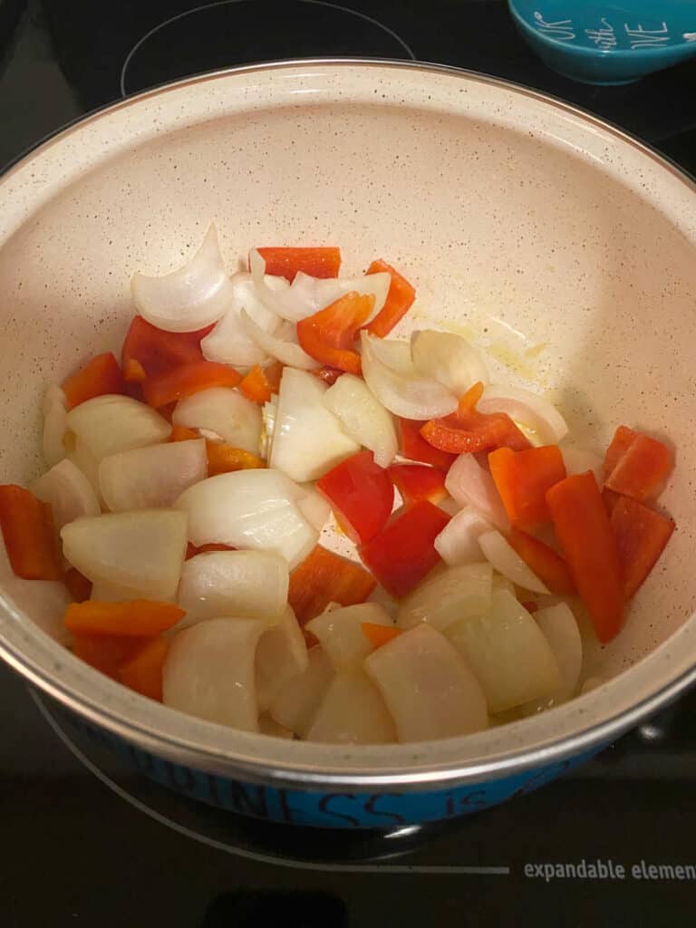 Process shot - bell pepper and onion cooking in pot. 