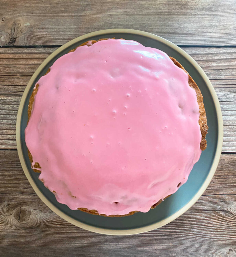 Glazed cake sits on a blue plate on a wooden background. 