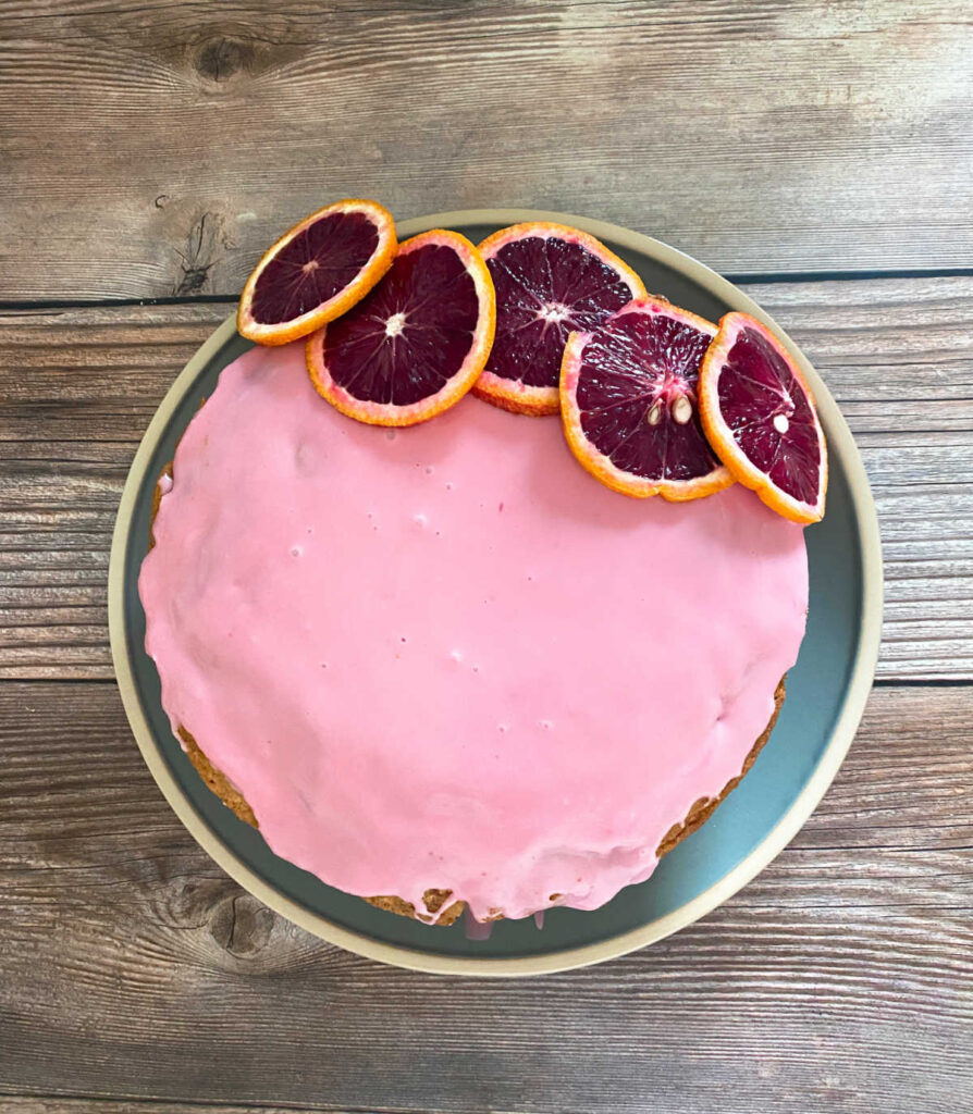 Glazed cake, topped with blood orange slices, sitting on a blue plate.