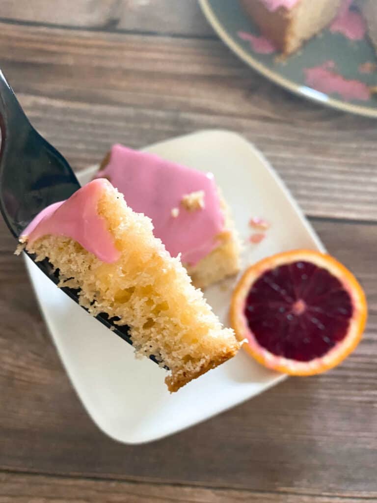 Forkful of cake is held above the slice of cake on a white square plate. 