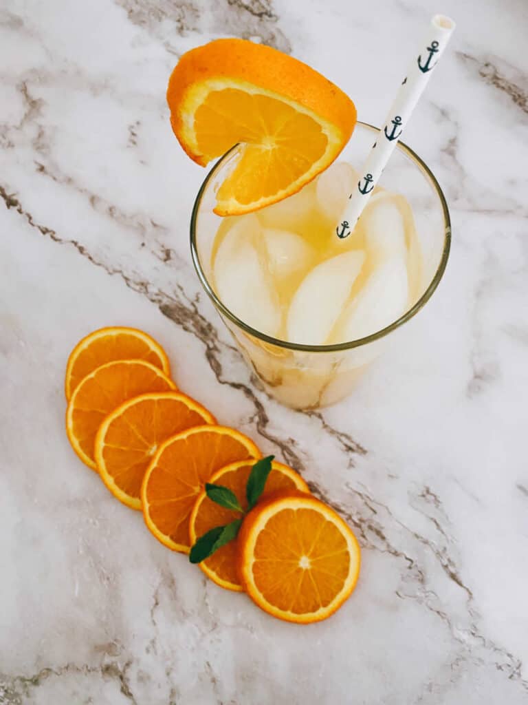 overhead image of cocktail in a glass on a marble background with orange slices. 