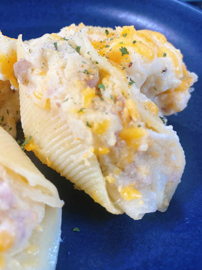 Close up image of stuffed shells on a dark blue plate, to show the filling. 