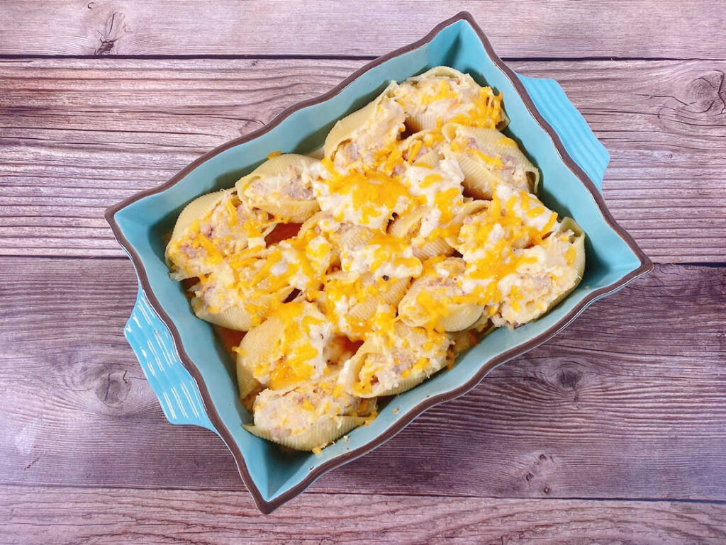 Turquoise baking dish full of the stuffed shells sits on a wooden background. 