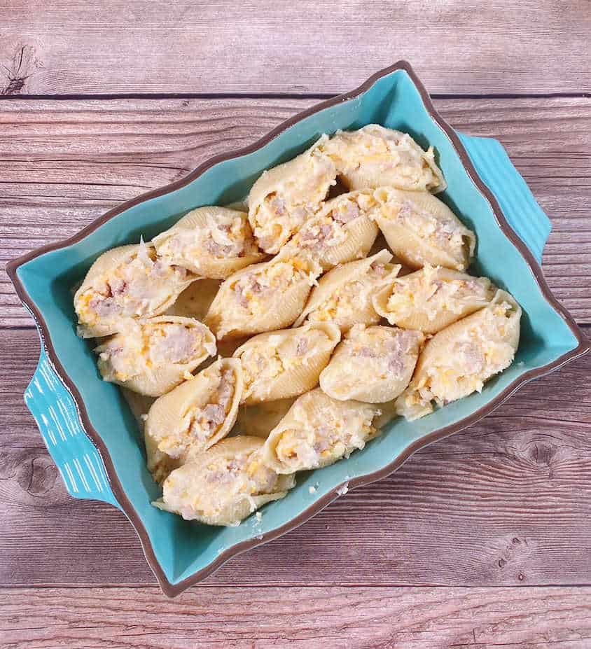 Process shot - stuffed shells in turquoise baking dish ready to be baked. 