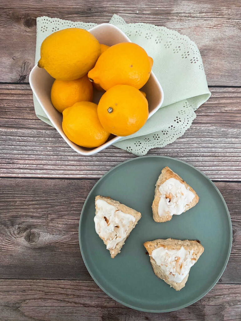 scones sit on a green plate on a wooden background. Bowl of lemons sits off to the side.
