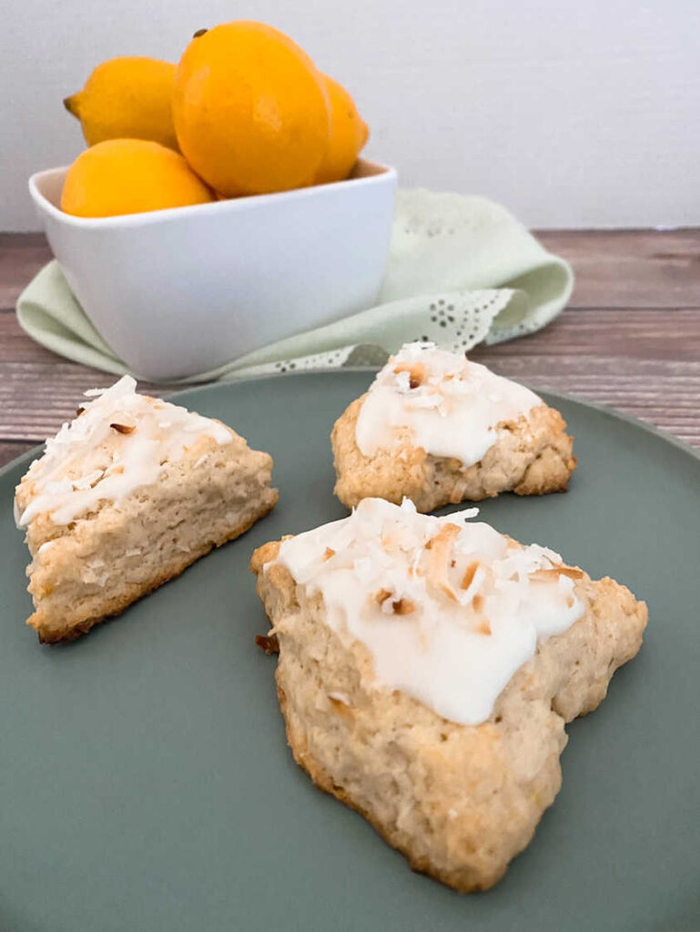 Three scones on a green plate with a bowl of lemons in the background. 