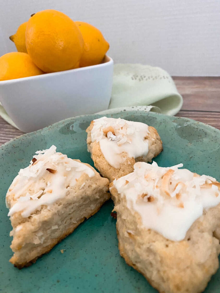 Close up image of three scones on a scalloped plate with a bowl of lemons in the background. 