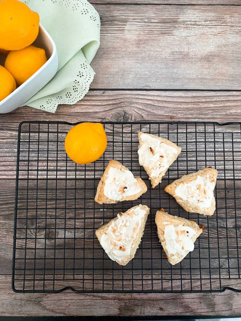 Overhead image of glazed scones sitting on a wire rack with a bowl of lemons in the background. 