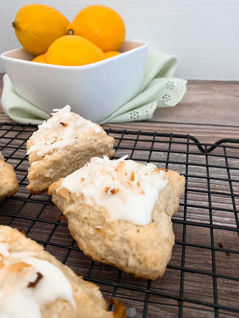 Scones siting on a wire rack with a bowl of lemons in the background. 