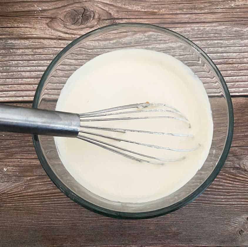 Process shot - wet ingredients in a glass bowl whisked together, with whisk still in bowl. 