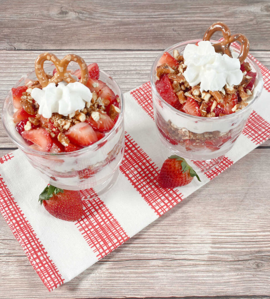 Overhead image of two parfaits in mini trifle cups sitting on a red and white printed towel, garnished with strawberries.