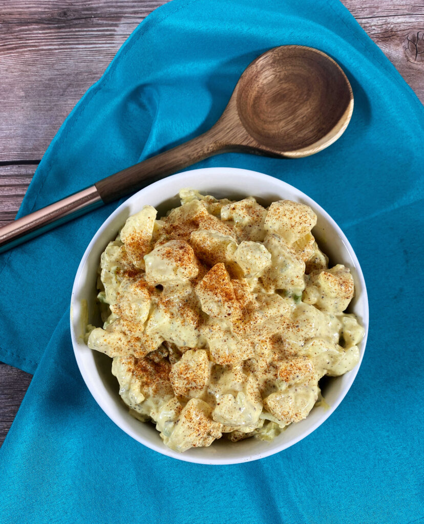 overhead image of potato salad in a white bowl with a wooden serving spoon. 