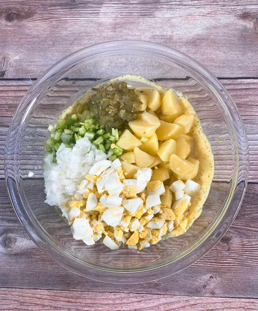 Prep image- potatoes, celery, onion and egg added to the sauce in a glass bowl. 