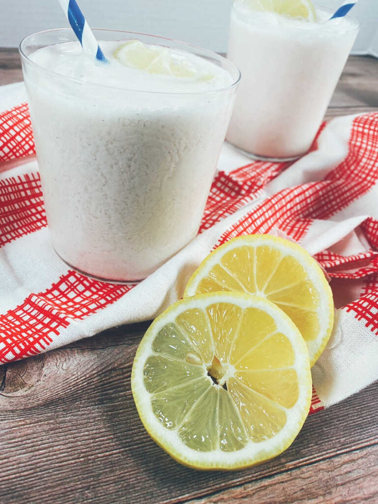 Drink in glasses on red and white napkin with blue striped straw and lemon slices as garnish.