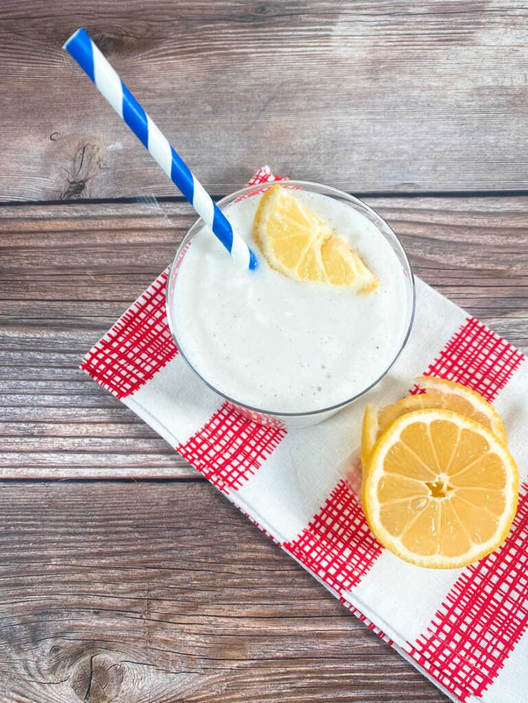 Drink sits on red and white printed napkin, with lemon slices as a garnish.