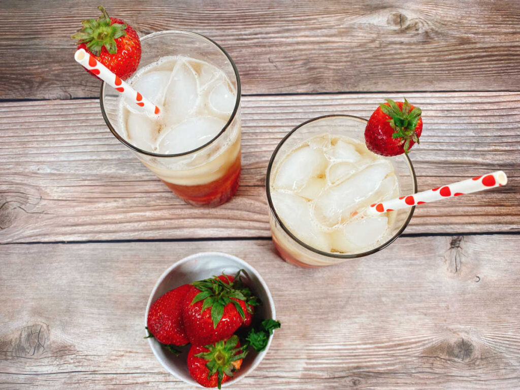 overhead image of cocktails, garnished with strawberries in tall glasses on a wooden background. 