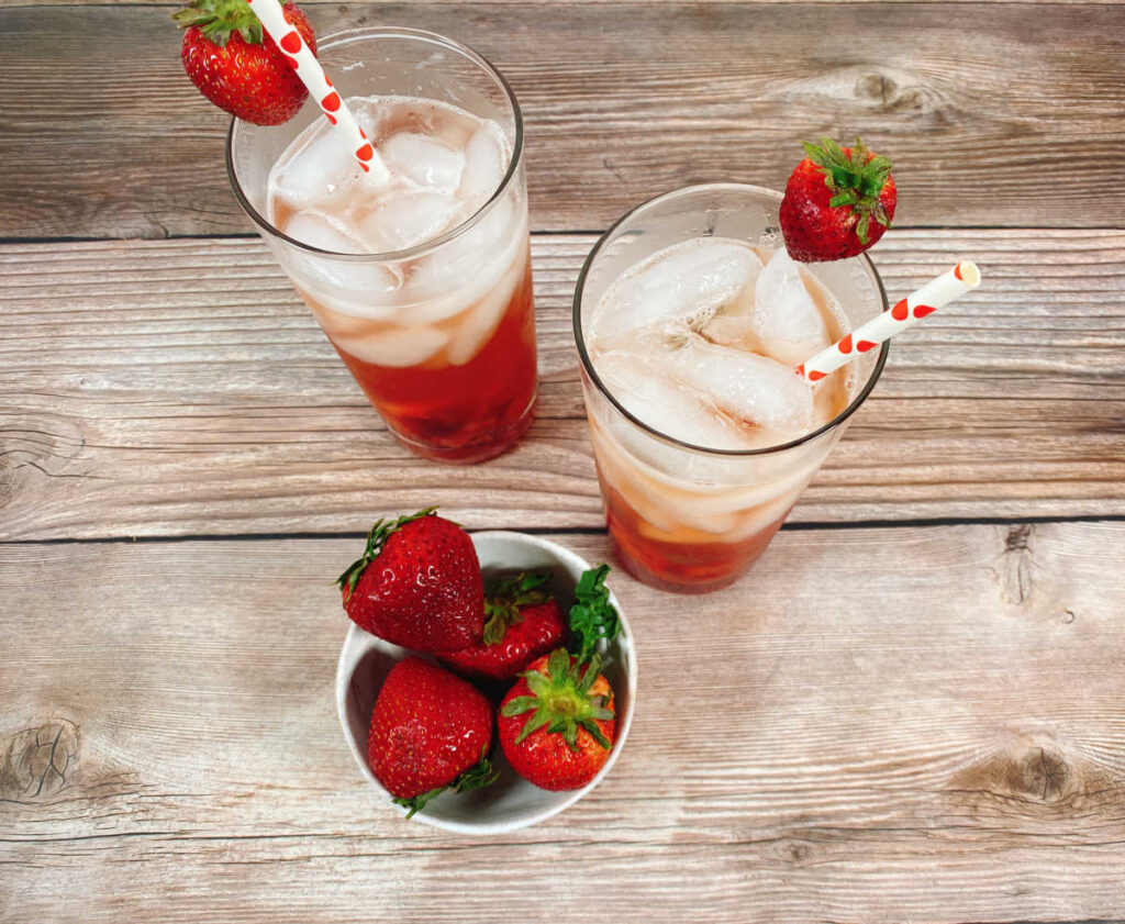 overhead image of two cocktails and a bowl of strawberries on a wooden background. 