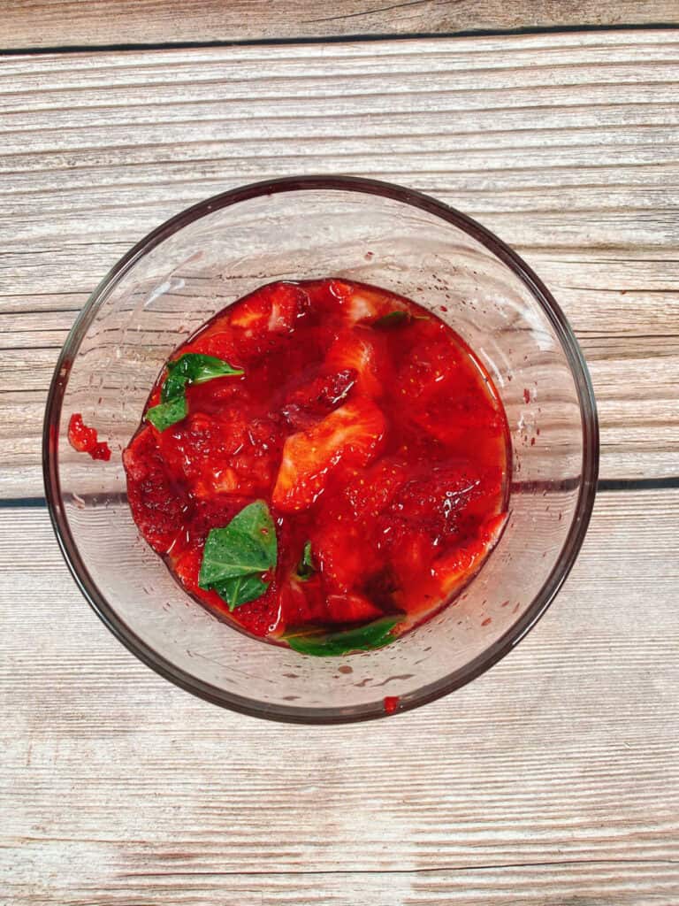 prep image - muddled strawberries and basil in a glass bowl. 