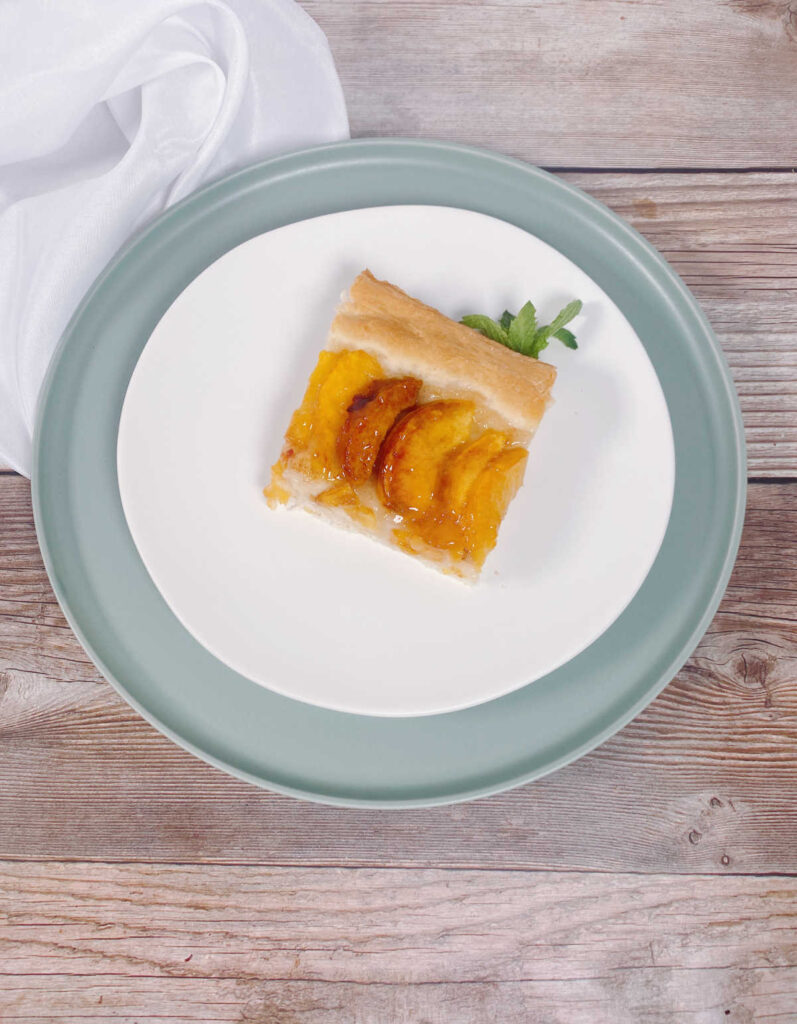 Slice of cake sits on a white round plate, stacked on top of a light green plate on a wooden background. 