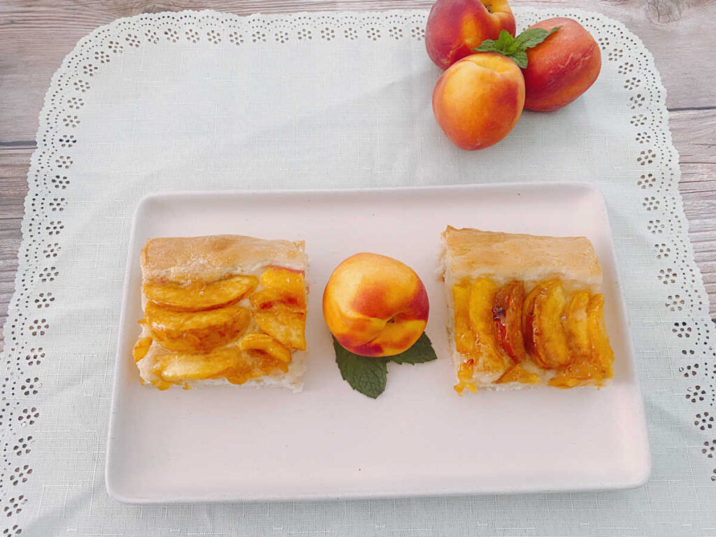 Slices of cake sit on a pink rectangle platter. A peach sits on a bed of fresh mint between the slices. 
