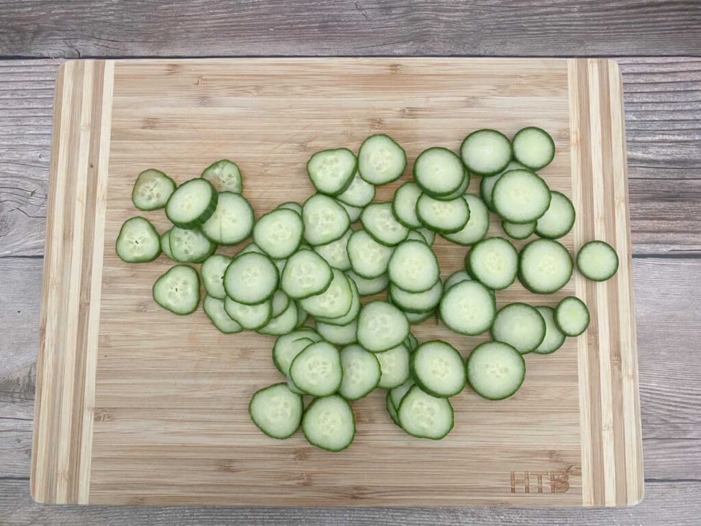 Process shot - thinly sliced cucumber rounds on a cutting board. 
