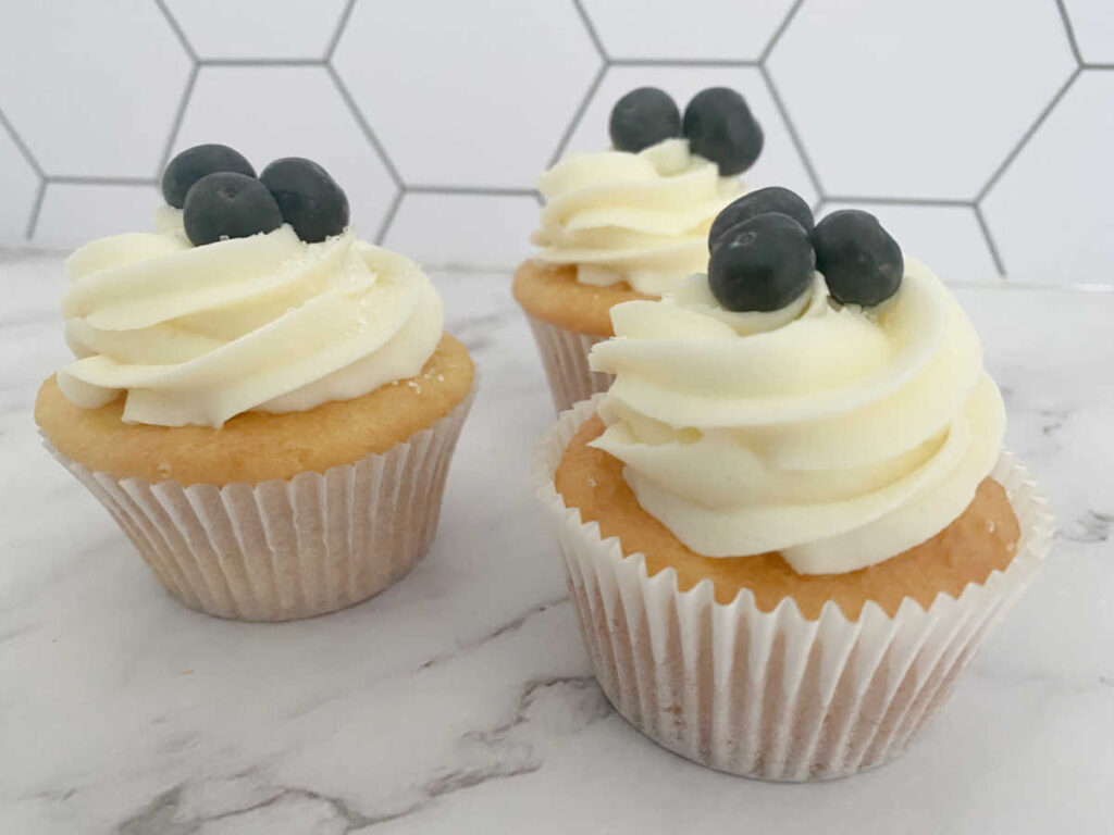 frosted and garnished cupcakes sit on a marble background.