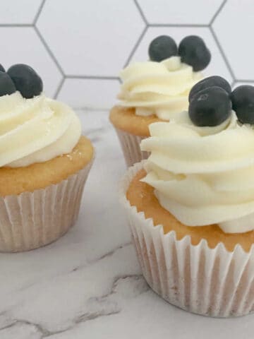 frosted and garnished cupcakes sit on a marble background.