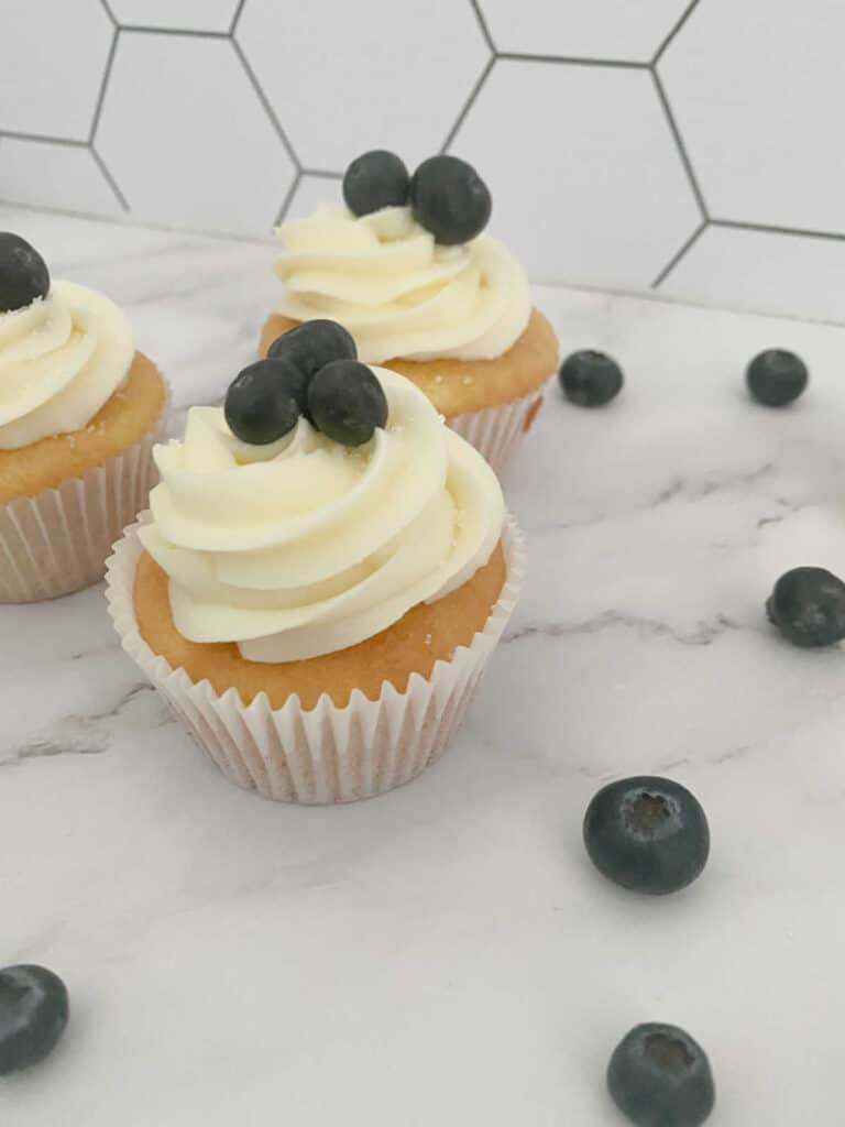 Cupcakes sit on a marble background with fresh blueberries around them.