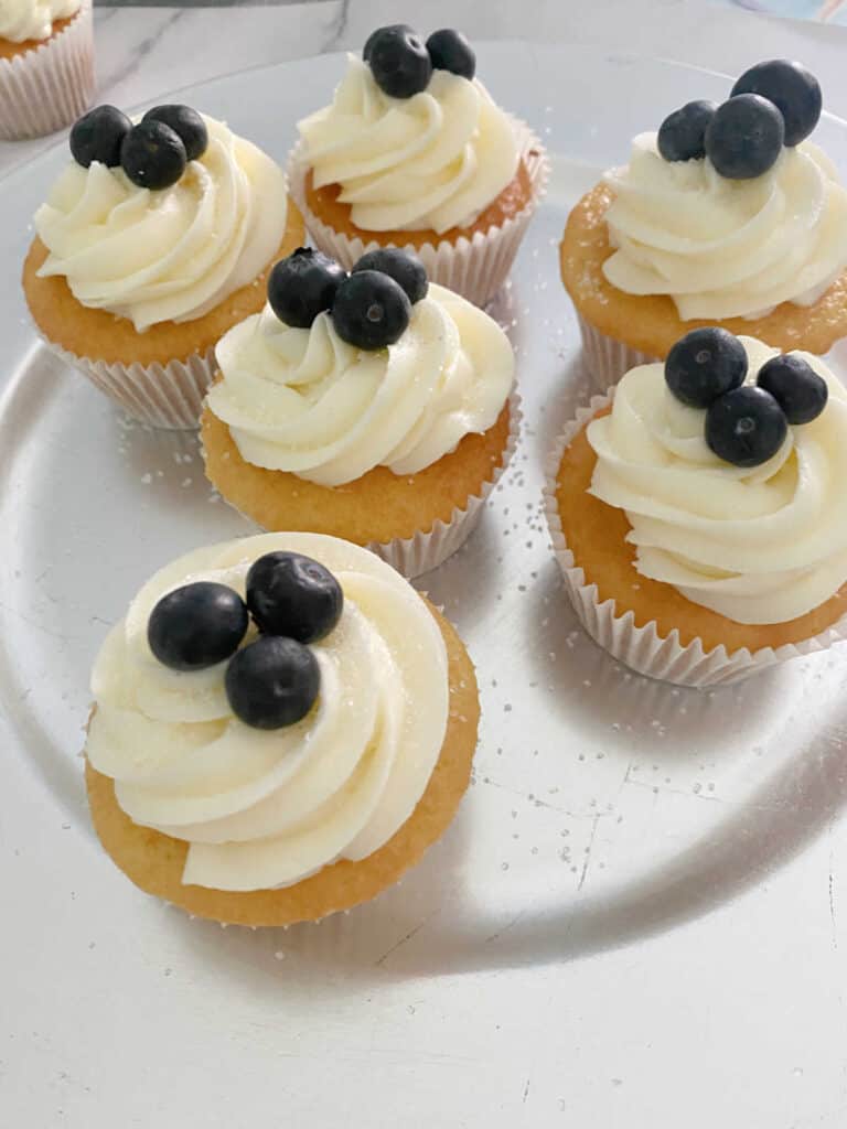 process shot - frosted and garnished cupcakes sit on a silver dish. 