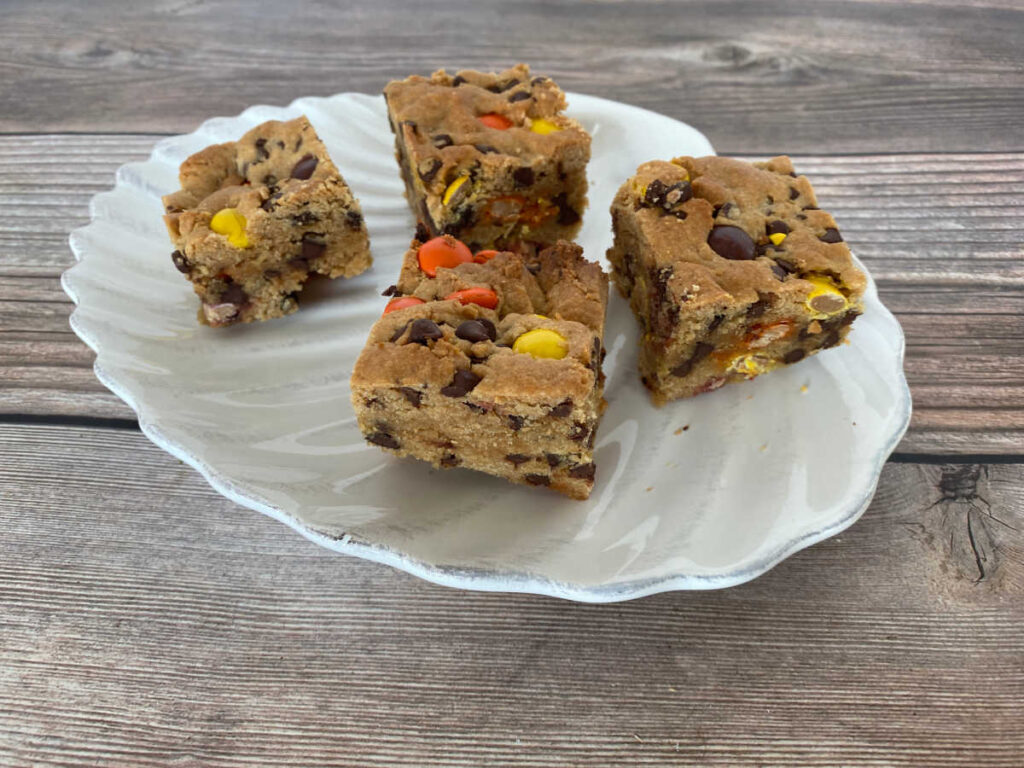 Cookie bars are spaced out on a white scalloped plate on a wooden background. 