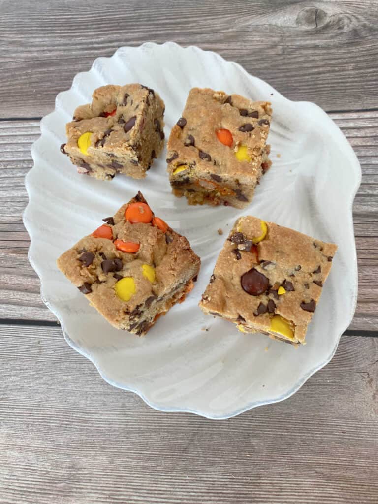 Cookie bars are spaced out on a white scalloped plate on a wooden background. 