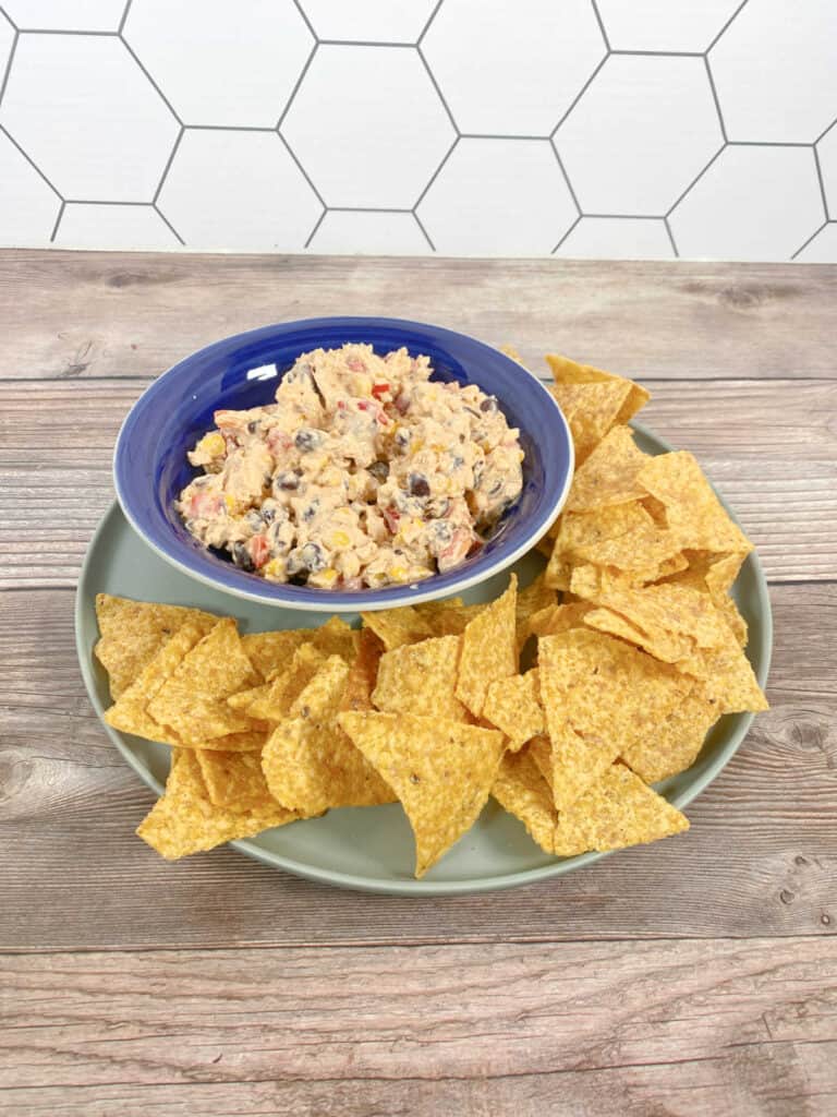 Dip in a blue bowl surrounded by tortilla chips on a wooden background.
