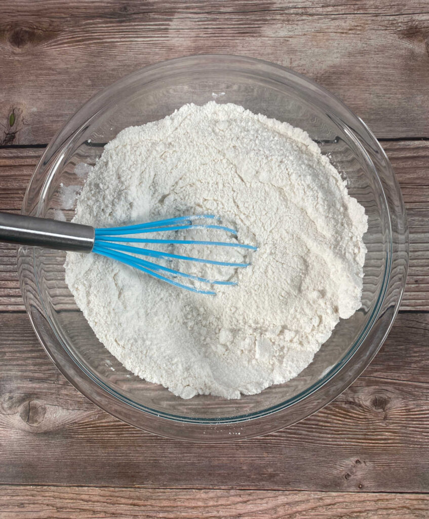 Process shot - dry ingredients in a glass bowl with a blue whisk. 