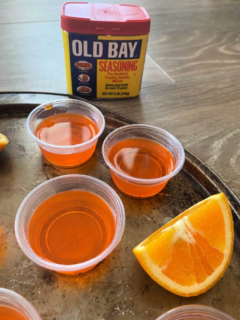 Close up image of jello shots on a round pan, with a slice of orange next to them.